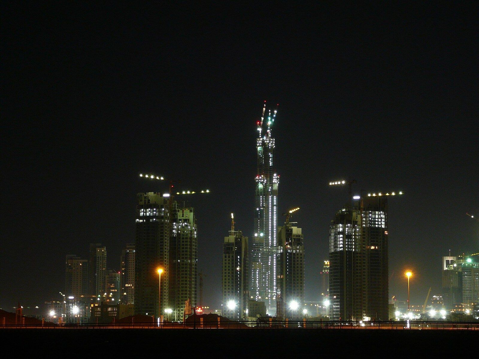 Towers under construction lit at night with cranes at their tops, a Wikimedia Commons photograph in Michael Stern's encyclopedia
