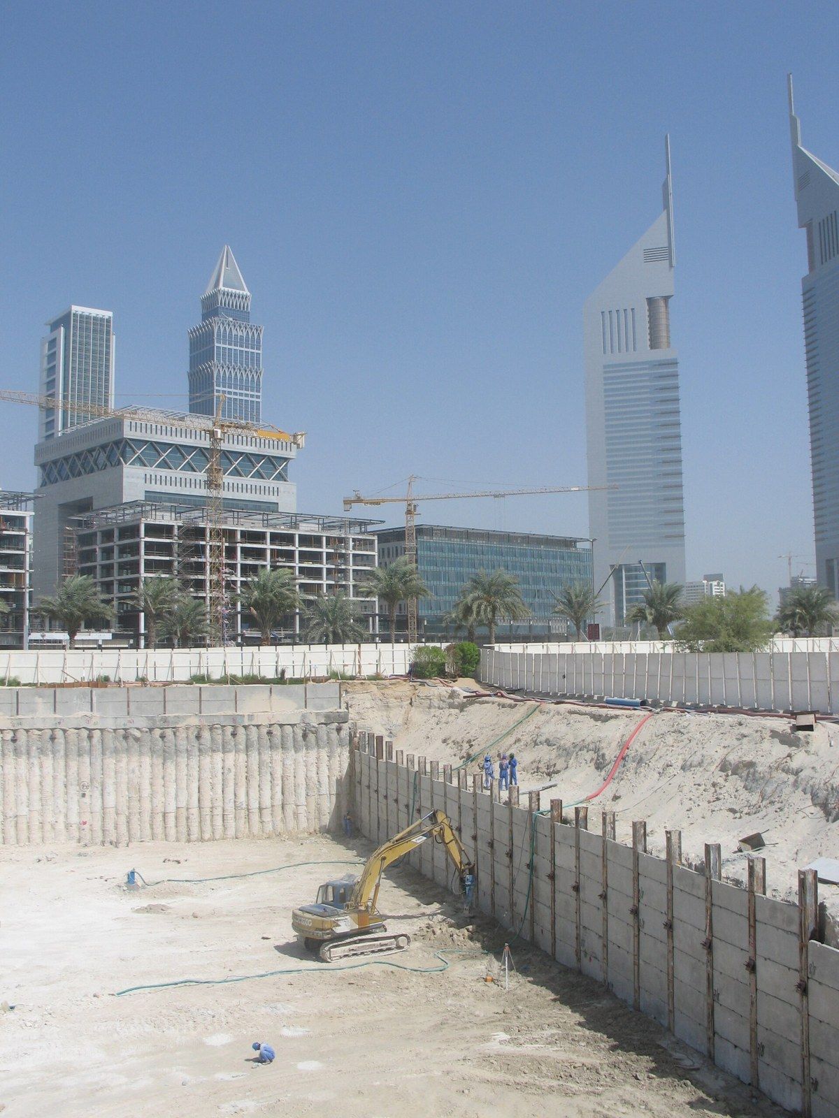 A deep excavation with a piled retaining wall and an excavator, towers behind, a Wikimedia Commons photograph in Michael Stern's encyclopedia