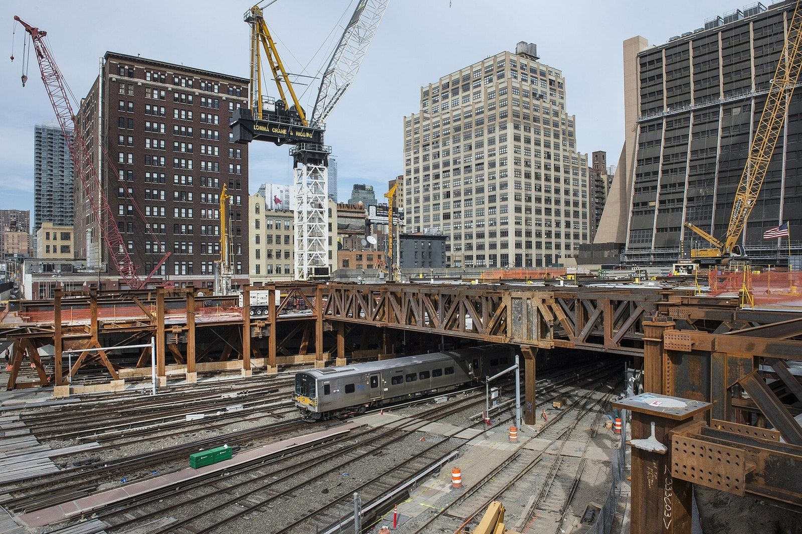 Cranes and a steel platform being built above active rail tracks with a train passing beneath, a Wikimedia Commons photograph in Michael Stern's encyclopedia