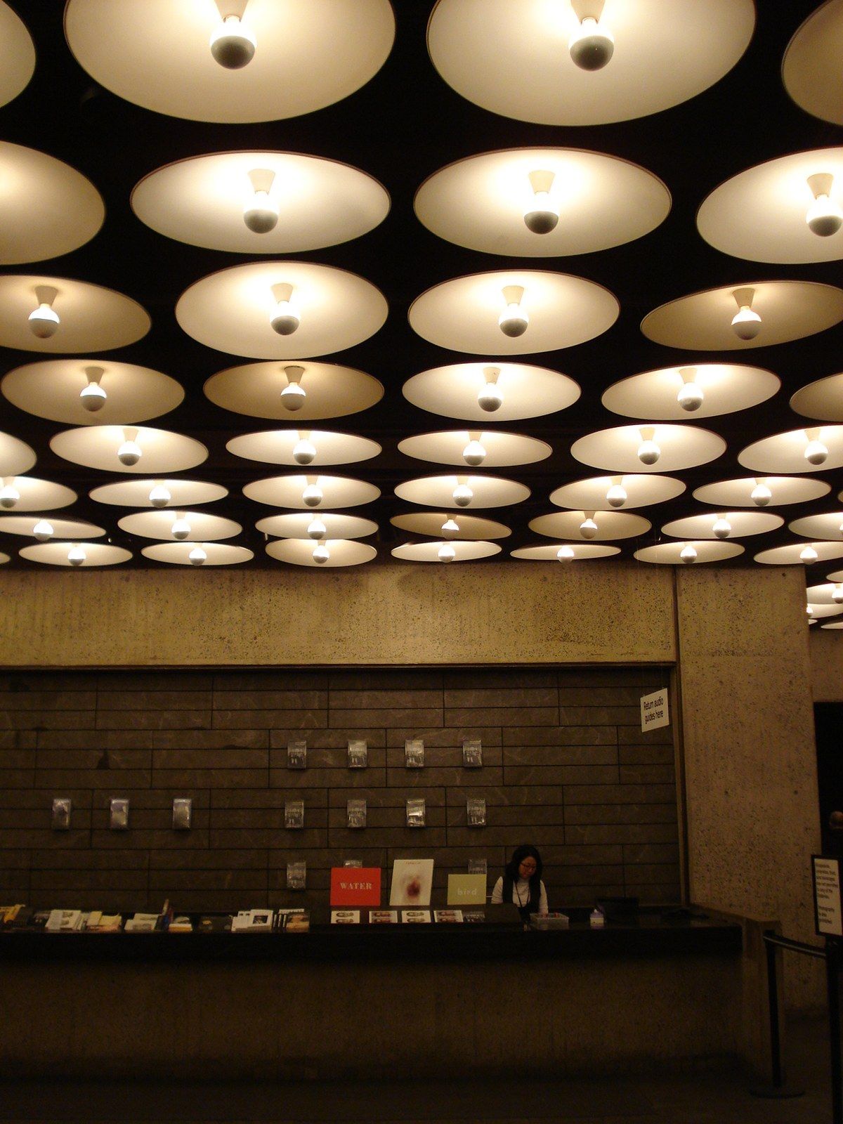 A museum lobby with a ceiling of round recessed lights and a stone desk, a Wikimedia Commons photograph in Michael Stern's encyclopedia