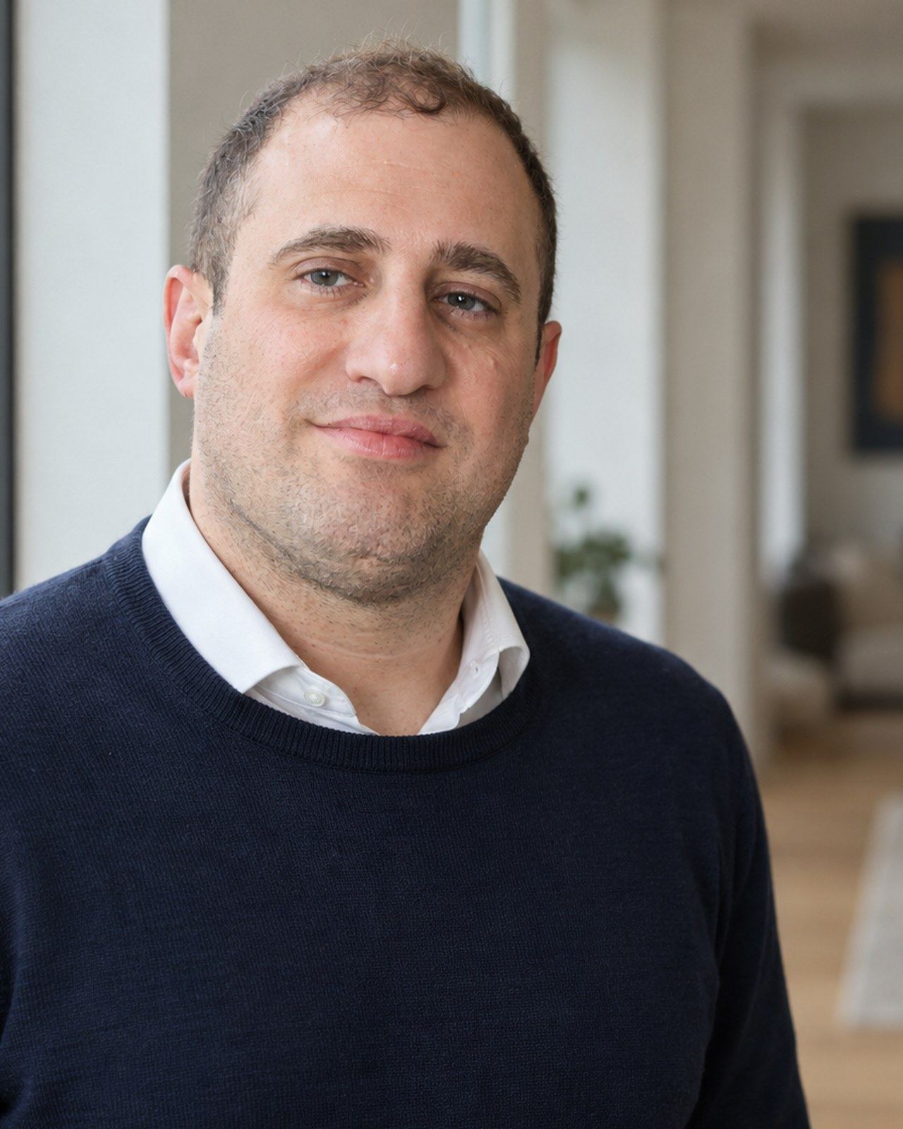 Michael Stern in a dark sweater and open collar shirt, seated by a window with daylight across the room