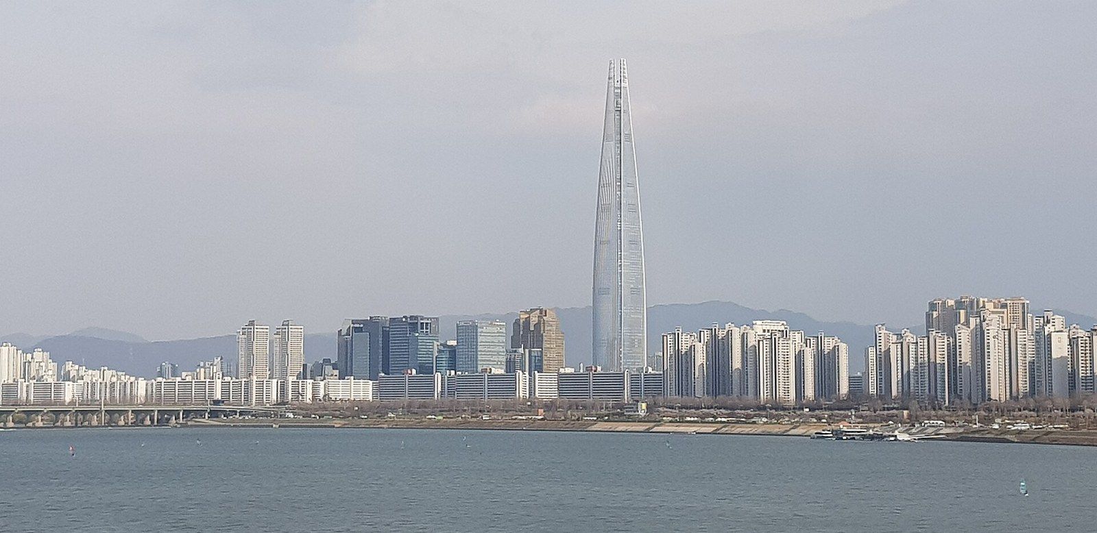 A tapering supertall tower rising above a river and a city skyline in haze, a Wikimedia Commons photograph in Michael Stern's encyclopedia