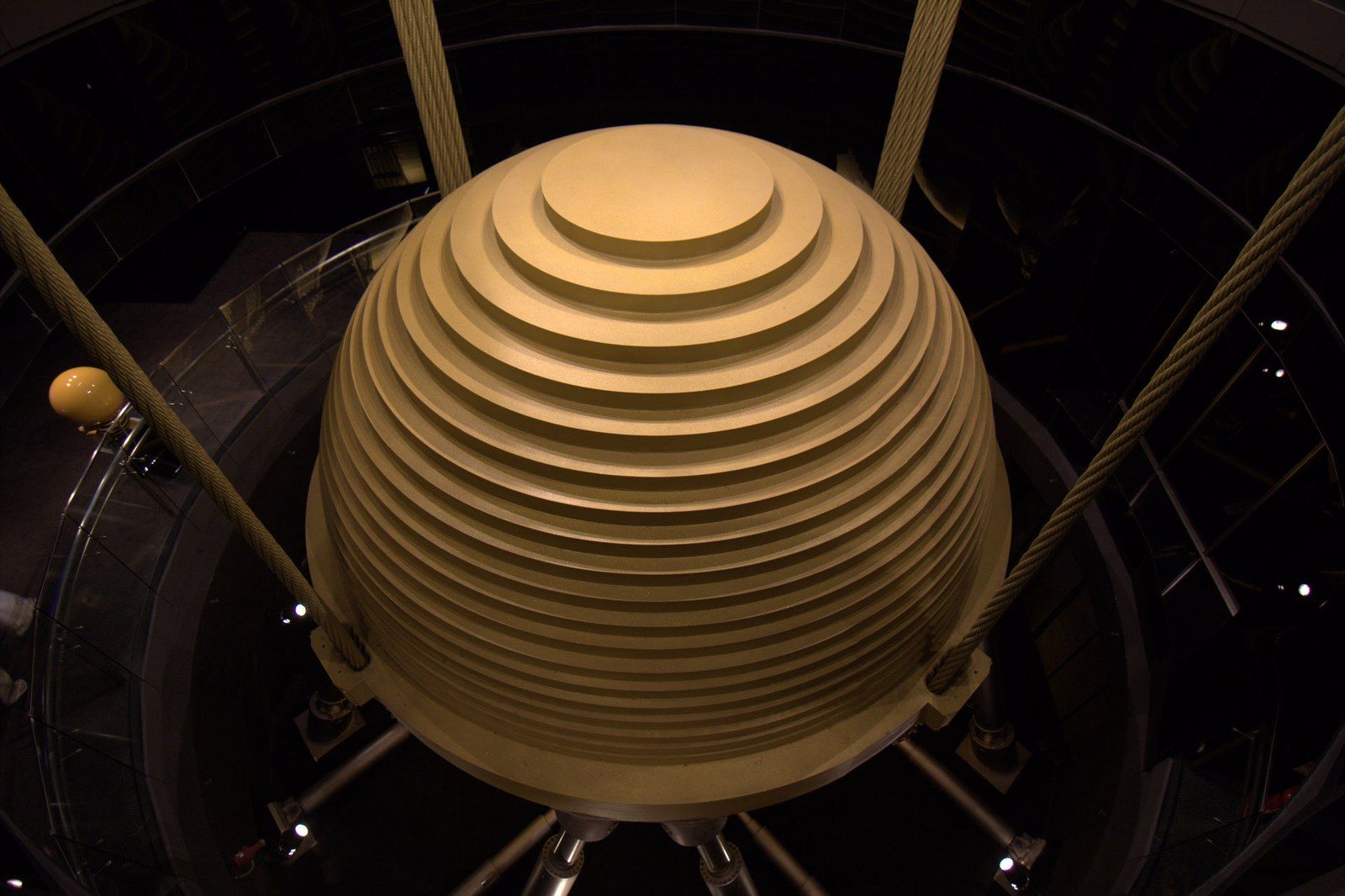 A ribbed golden damper sphere hanging on cables, seen from below, a Wikimedia Commons photograph in Michael Stern's encyclopedia