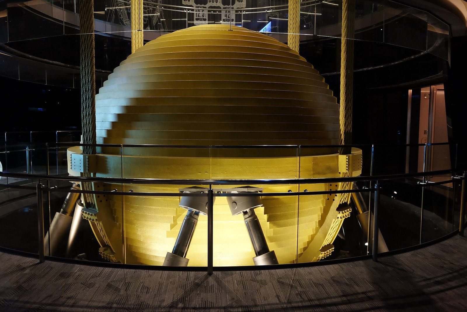 A gold painted steel sphere suspended on cables inside a tall building, seen from an observation deck, a Wikimedia Commons photograph in Michael Stern's encyclopedia